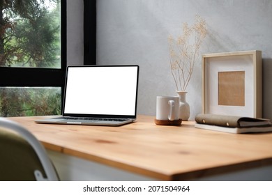 Computer laptop with blank display, pencil holder, coffee cup and houseplant on wood table.