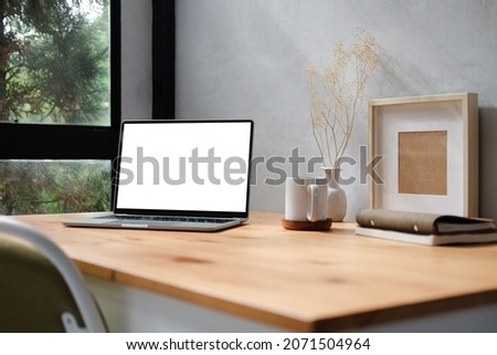 Computer laptop with blank display, pencil holder, coffee cup and houseplant on wood table.