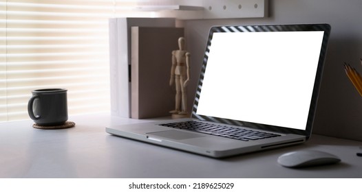 Computer Laptop With Empty Screen, Books, Coffee Cup And Pencil Holder On White Table In Bright Living Room.