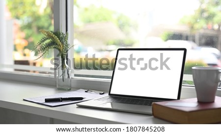 A computer laptop with a white blank screen is putting on a windowsill surrounded by various equipment.