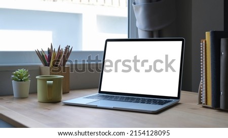 Computer laptop with white empty screen, coffee cup and stationery on wooden table.