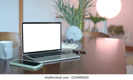 Computer laptop with white screen, smart phone and glasses on wooden office desk.