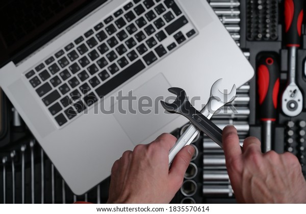 computer maintenance repair\
concept of man technician holding in hands chrome socket wrench\
spanner on background with silver laptop on auto toolbox kit in\
workshop