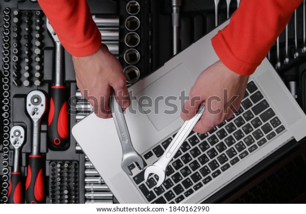 computer maintenance repair\
concept of man technician holding in hands chrome socket wrench\
spanner on background with silver laptop on auto toolbox kit in\
workshop