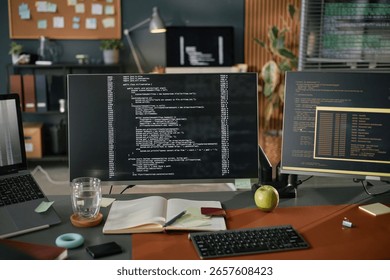 Computer monitor displaying programming code on desk with notebook, pen, glass of water, apple, and sticky notes, suggesting software development or coding workspace in modern office