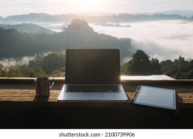 Computer Monitor, Keyboard, coffee cup and Mouse with Blank is on the work table at the sky mountain river and trees front view background.