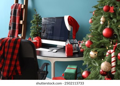 Computer monitor with Santa hat, cocoa and Christmas tree on programmer's desk in office - Powered by Shutterstock