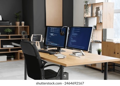 Computer monitors with programming code and headphones on desk in office