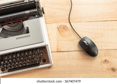 Computer mouse connected to an old typewriter on wooden background