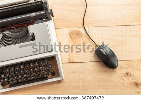 Computer mouse connected to an old typewriter on wooden background