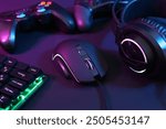 Computer mouse, headset, RGB keyboard and game controllers in neon lights on dark background, closeup