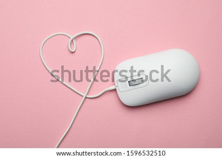Computer mouse with heart shaped wire on pink background, top view