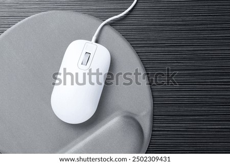 Computer mouse and mousepad with armrest on black wooden table, top view. Space for text