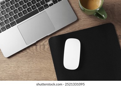 Computer mouse with mousepad, laptop and cup of coffee on wooden table, flat lay