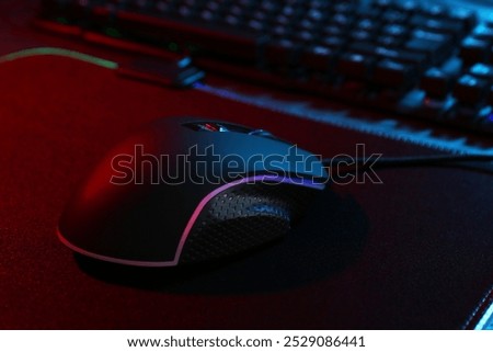 Computer mouse and mousepad on table in neon lights, closeup