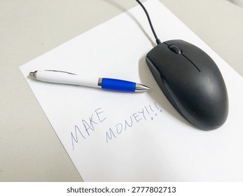 Computer mouse and pen resting on white paper with words make money written in blue ink