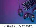 Computer mouse, RGB keyboard and game controllers in neon lights on dark background, flat lay. Space for text