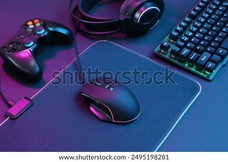 Computer mouse, RGB keyboard, game controller and headset in neon lights on dark background
