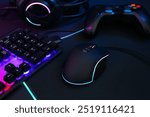 Computer mouse, RGB keyboard, headset and game controller on dark background, closeup