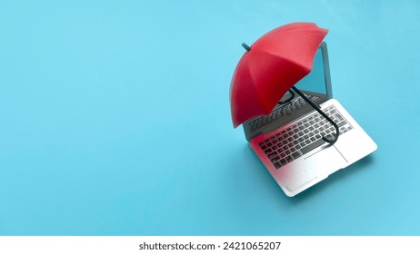 Computer and network security concept. Red umbrella cover the laptop over a blue background.