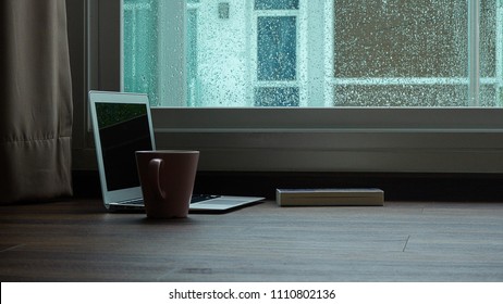 computer notebook next to a cup coffee  on rainy day window background