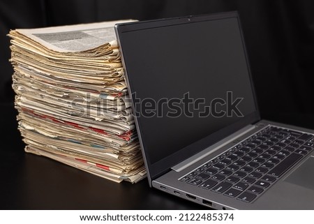 Computer notebook and a pile of newspapers on a table
