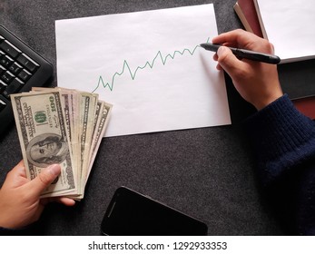 computer numeric keypad, graphic with ascending line, ballpoint pen, books, business man hands and american banknotes