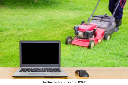 Computer on the table , blur image of man cutting grass field as background.