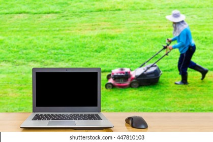 Computer on the table , blur image of man cutting grass field as background.