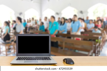 Computer on the table, blur image of inside the church as background.