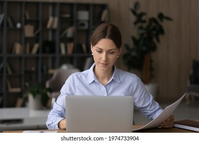 Computer and papers. Focused millennial woman office worker teacher freelancer do paperwork manage legal documents fill in electronic form. Young lady lawyer study text of contract agreement by laptop - Shutterstock ID 1974733904