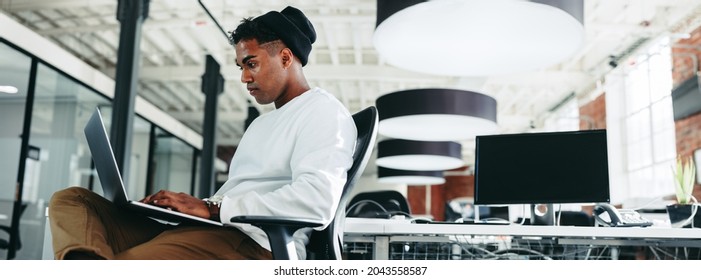 Computer programmer working on a new code in an office. Focused young businessman using a laptop while sitting in a modern workplace. Creative businessman working alone during the day.