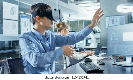 Computer Science Engineer wearing Virtual Reality Headset Works with 3D Modeling, Makes Gestures. In the Background Engineering Bureau with Busy Corowrkers.