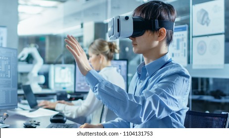 Computer Science Engineer wearing Virtual Reality Headset Works with 3D Modeling, Makes Gestures. In the Background Engineering Bureau with Busy Coworkers.