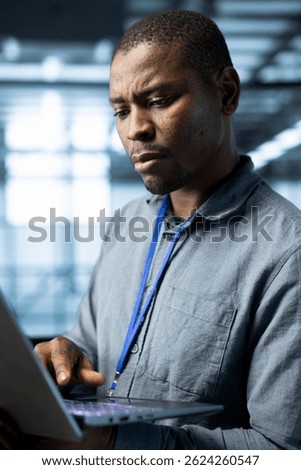 Computer scientist in data center using laptop to develop disaster recovery plans. African american man in server hub testing failover scenarios using notebook, protecting data during disruptions