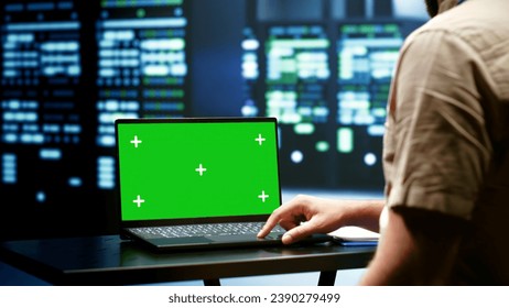 Computer scientist monitoring mainframes doing intense computations. Programmer using green screen laptop to assess strain on server room rigs caused by AI applications driving up power usage - Powered by Shutterstock