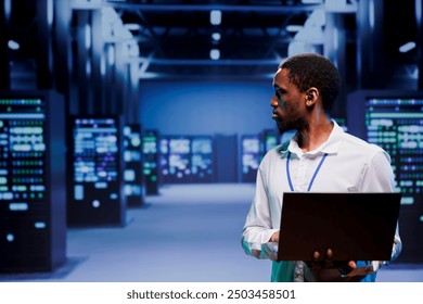 Computer scientist strolling amidst data storage devices in server room, ensuring proper operational conditions. Repairman closely monitoring energy consumption of high tech facility infrastructure - Powered by Shutterstock