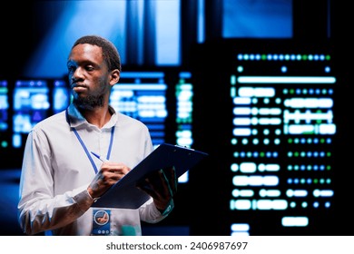 Computer scientist using clipboard to note changes to server rigs performing data backups and providing centralized storage. Expert reviewing Uninterruptible Power Supply ensuring proper functioning