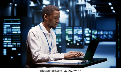 Computer scientist using laptop to debug servers cabinets helping companies manage databases, host websites and store files. Repairman reviewing high tech facility used for high performance computing