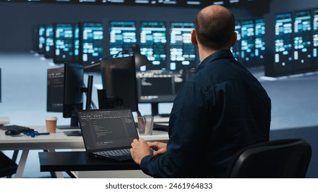 Computer scientist using laptop device to do programming in data center room housing servers . IT supervisor writing code on notebook to mend data storage facility racks doing computational operations