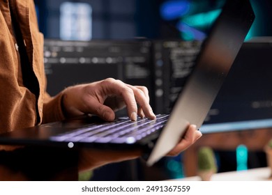 Computer scientist working from home using laptop, testing and deploying programs. Programmer checking code displayed on desktop PC screens in blurry background, close up shot