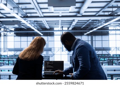 Computer scientists in data center tracking network traffic and activity, installing and configuring software updates. Coworkers performing database backups on notebook to protect user information