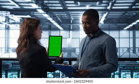 Computer scientists in data center use mockup tablet, inspecting server rigs, updating devices. Teamworking IT colleagues collaborating to ensure stable operations, using chroma key device, camera B