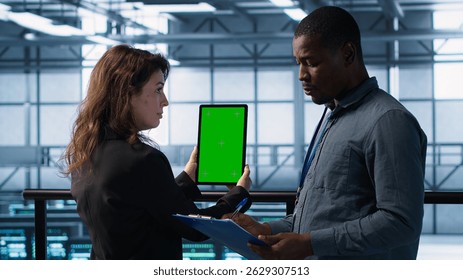 Computer scientists in data center use mockup tablet, inspecting server rigs, updating devices. Teamworking IT colleagues collaborating to ensure stable operations, using chroma key device, camera A