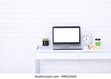 Computer screen with copy space and notebooks near brick wall. Cup of coffee and retro clock