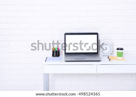 Computer screen with copy space and notebooks near brick wall. Cup of coffee and retro clock