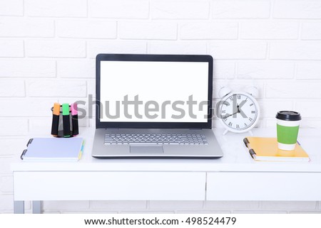 Computer screen with copy space and notebooks near brick wall. Cup of coffee and colorful markers