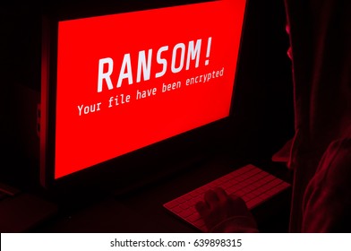 Computer screen with ransomware attack alert in red and a man keying on keyboard in a dark room, ideal for online security and digital crime - Shutterstock ID 639898315