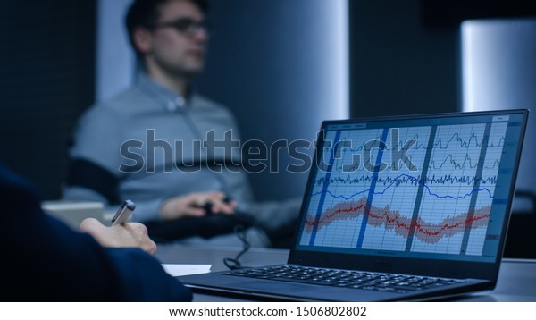 Computer Shows Physiological Measures of a\
Man Undergoing Lie Detector / Polygraph Test. Examining Expert\
Writes Down\
Observations.