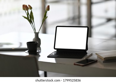 A computer tablet with a white blank screen is putting on a working desk surrounded by various equipment.